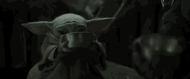 a baby yoda from star wars is holding a bowl of food in his hands .
