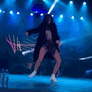 a woman in a black coat and white boots is dancing on a stage .