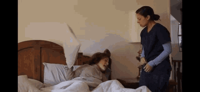 a woman in scrubs is standing next to a woman laying in bed