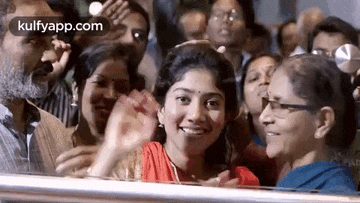 a group of people are standing around a woman who is smiling and waving at the camera .