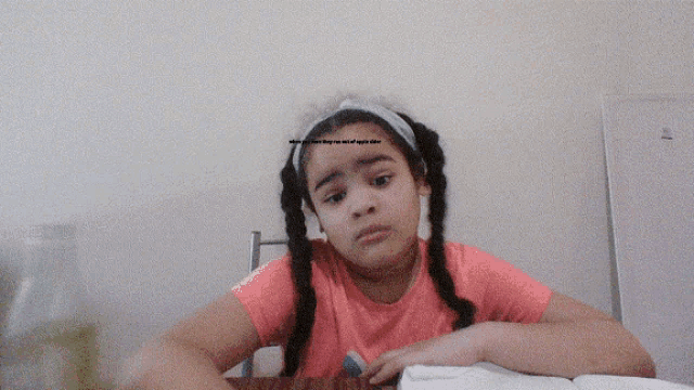 a little girl with braids sits at a table with an open book