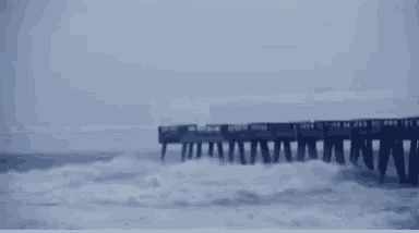 a train is going over a bridge in the snow with a reflection of it in the water .