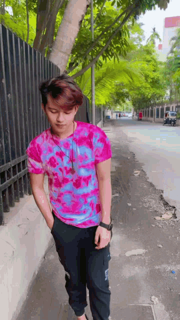a young man wearing a pink and blue shirt is walking down a sidewalk