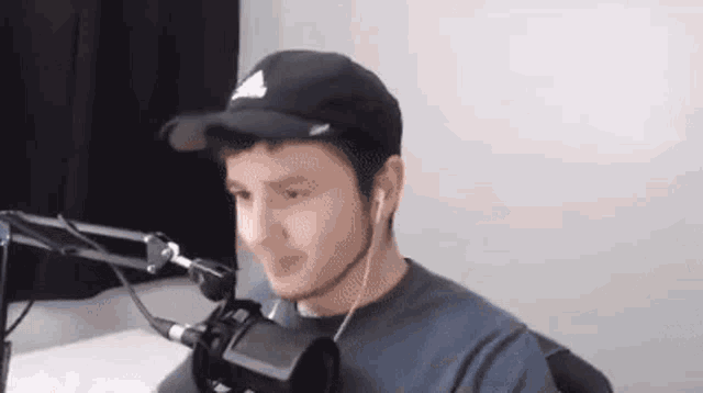 a young man wearing a hat and ear buds is sitting in front of a microphone .