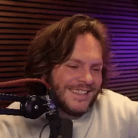 a man with a beard and long hair is smiling in front of a microphone .