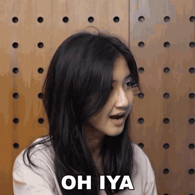 a woman with long black hair is making a funny face while standing in front of a wooden wall .