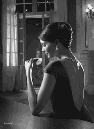 a woman in a dress is sitting at a table drinking from a cup .
