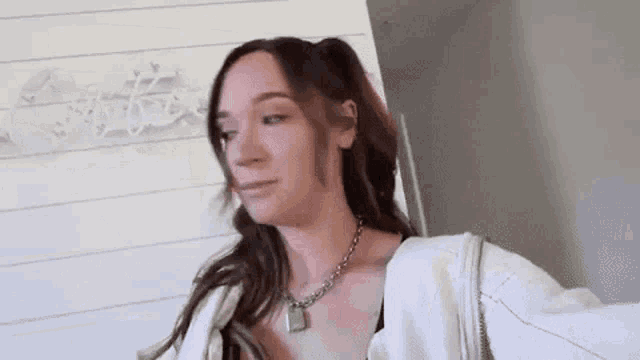 a woman wearing a necklace and a white jacket is standing in front of a door .