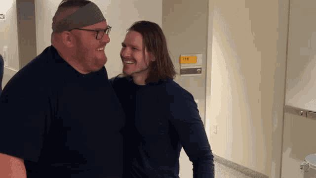 two men are standing next to each other in a hallway with a sign that says 119