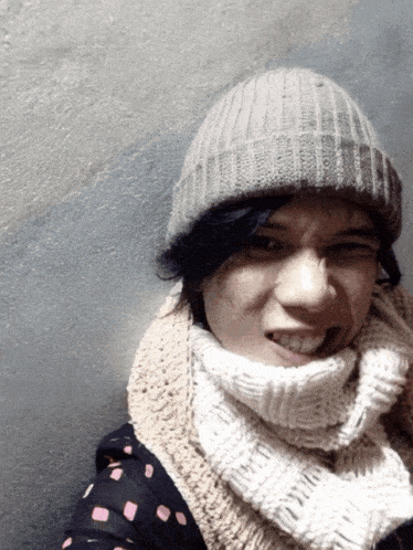 a woman wearing a scarf and a beanie smiles at the camera