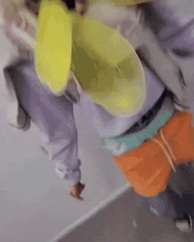 a person wearing a purple hoodie and orange shorts is holding a yellow object