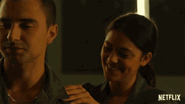 a woman adjusts a man 's shirt with a netflix logo in the background