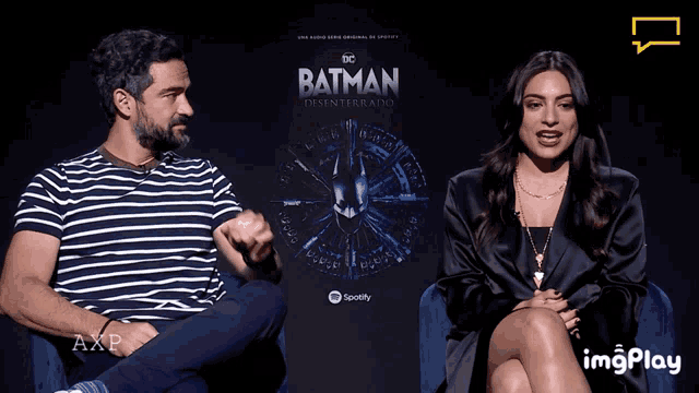 a man and a woman sit in front of a poster for batman