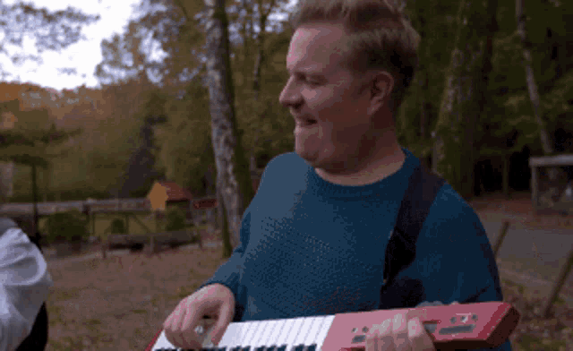 a man in a blue sweater is playing a keyboard in the woods