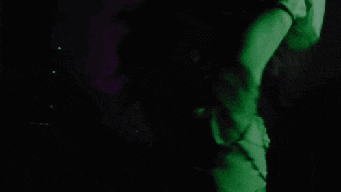 a woman is dancing in a dark room with a green light behind her