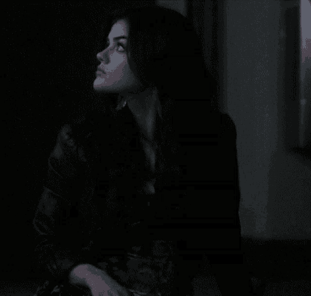 a woman in a black leather jacket is sitting in a dark room