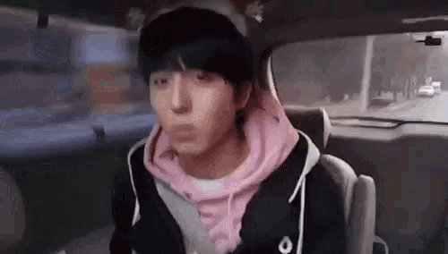 a young man is sitting in the back seat of a car wearing a pink hoodie and a pink hat .