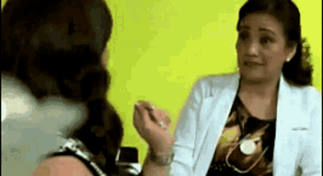 a woman in a white lab coat is talking to another woman in front of a yellow wall .