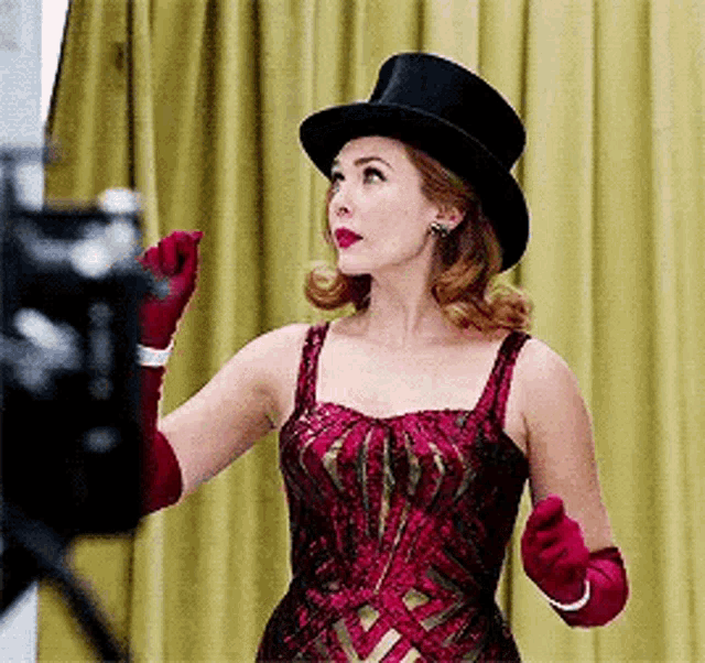 a woman wearing a top hat and gloves is standing in front of a yellow curtain .