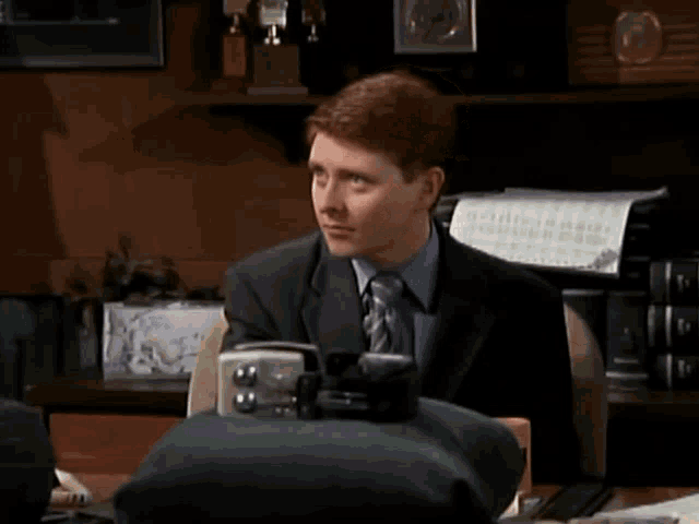 a man in a suit and tie is sitting at a desk with the words " and " written above him