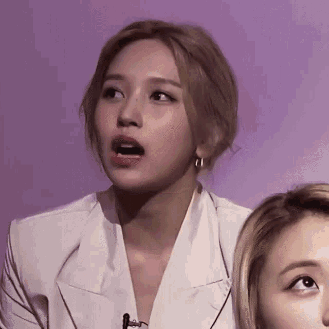 a woman in a white jacket is making a funny face next to another woman .
