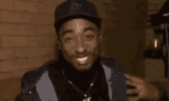 a close up of a man wearing a hat and smiling in front of a brick wall .