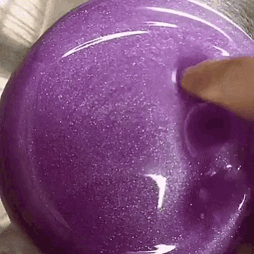 a person is playing with a purple slime with their finger .