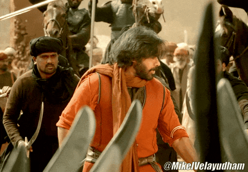 a man in a red shirt stands in a crowd with the name mikelvelayudham on the bottom