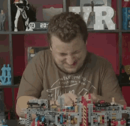 a man wearing a brown shirt that says welcome to is playing with lego