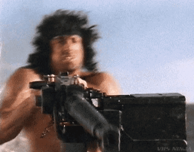 a man without a shirt is holding a machine gun in front of a blue sky .