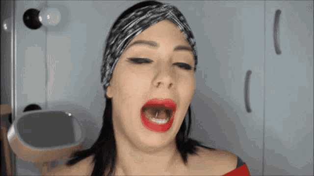 a woman wearing a headband and red lipstick is making a funny face with her mouth open .