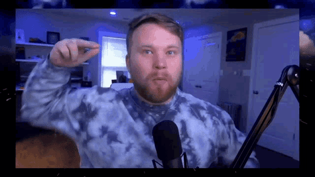 a man wearing a blue tie dye sweater is standing in front of a microphone