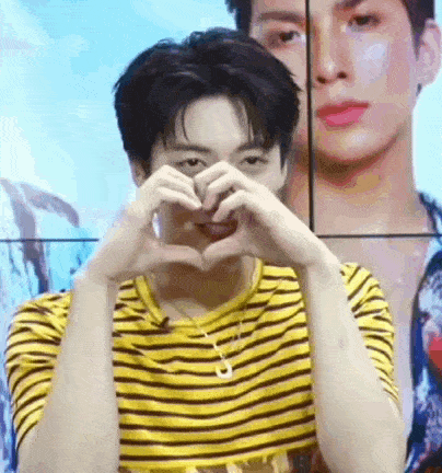 a young man in a yellow and black striped shirt is making a heart with his hands .