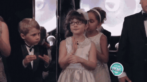 a little girl wearing glasses and a white dress is clapping her hands