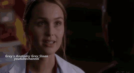 a close up of a woman in a white lab coat talking to a man in a dark room .
