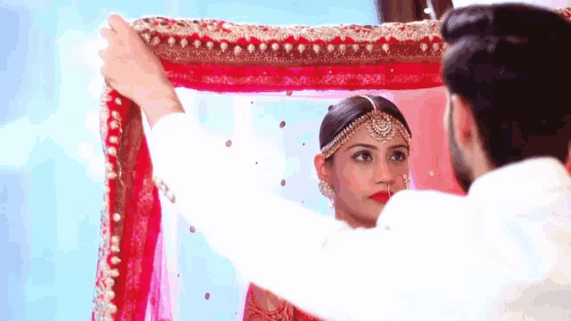 a man is holding a red and white cloth over a woman 's head
