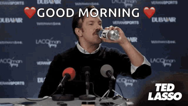 a man drinking water in front of a microphone with the words good morning behind him