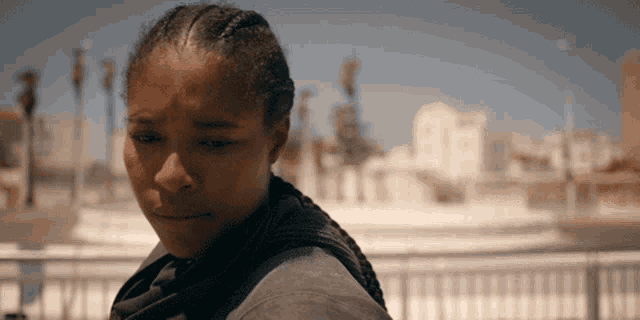 a woman with braids on her head looks at the camera with palm trees in the background