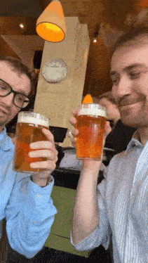 two men toasting with glasses of beer in front of a clock that says 12:37