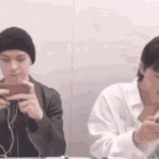 a man and a woman are sitting at a table looking at their phones .