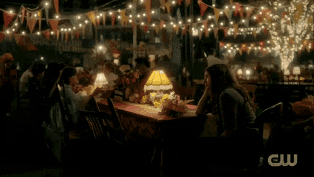 a woman sits at a table with a cw logo on the bottom right