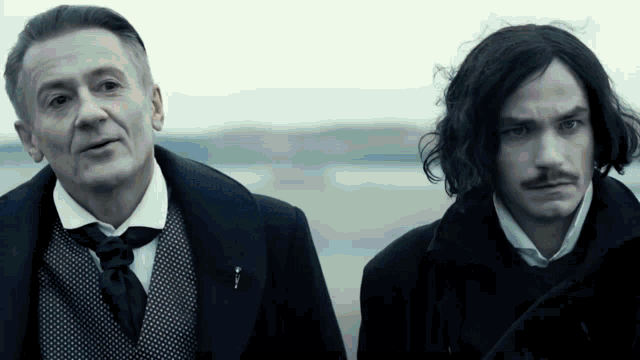 two men are standing next to each other and one of them has a pin on his jacket