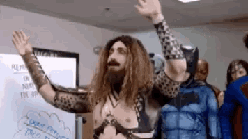 a man in a superhero costume is standing in front of a whiteboard with his arms in the air .