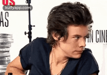 harry styles is wearing a black shirt and sitting in front of a stack of film .