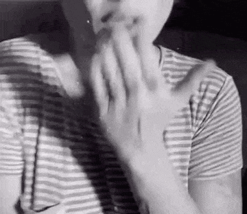 a black and white photo of a person wearing a striped shirt covering their mouth with their hands .