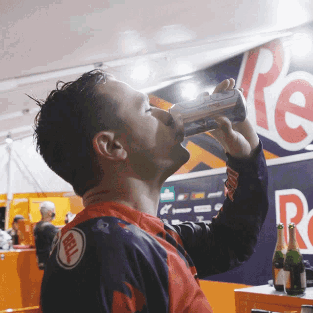 a man drinking from a can with a bell logo on his jersey
