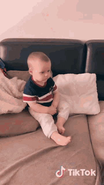 a baby is sitting on a couch with a tiktok sticker on the bottom