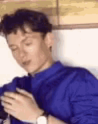 a man in a blue sweater is sitting in a chair looking at his phone .