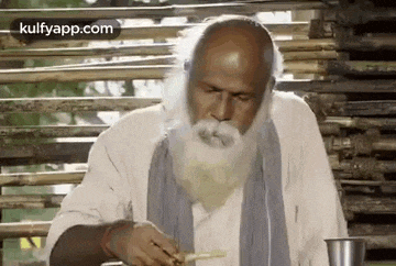 an elderly man with a beard is eating noodles with chopsticks .