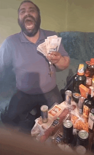 a man with a beard is holding a bunch of money in front of a table full of alcohol